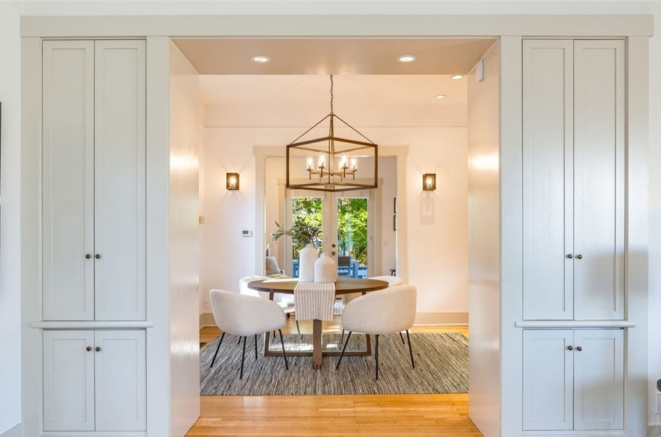 A bright dining room framed by white built-in cabinetry, with a round table and lantern chandelier